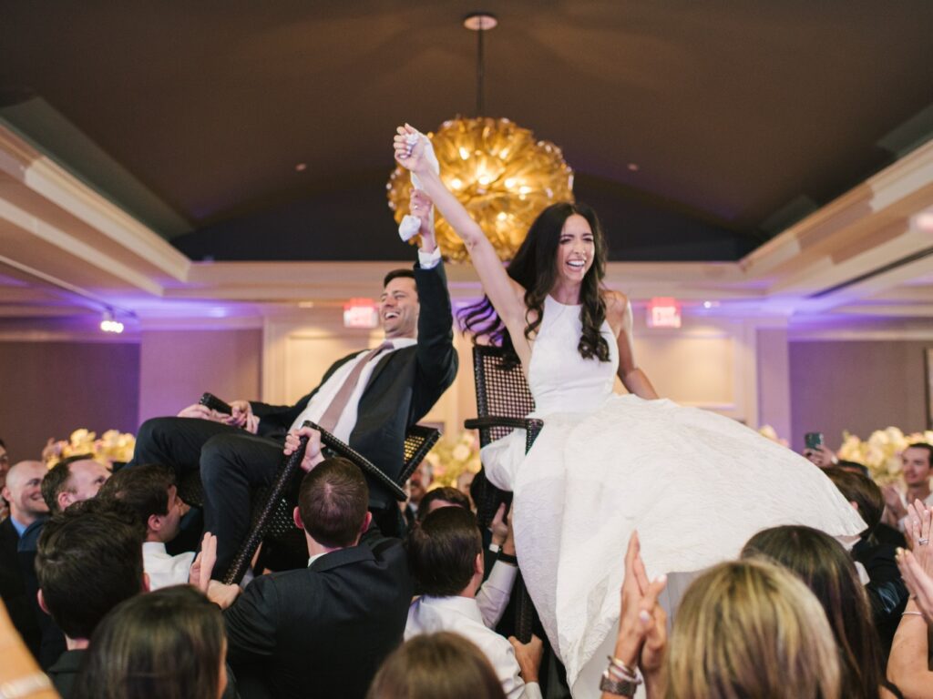 Brian and groom lifted up in chairs during the hora. The bride wears a lace halter gown by Lea-Ann Belter Bridal