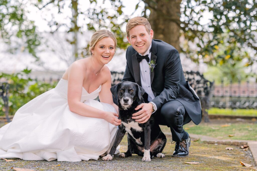 A bride and groom pose with their cute dog on their wedding day. The bride wears a strapless wedding dress by Astrid & Mercedes