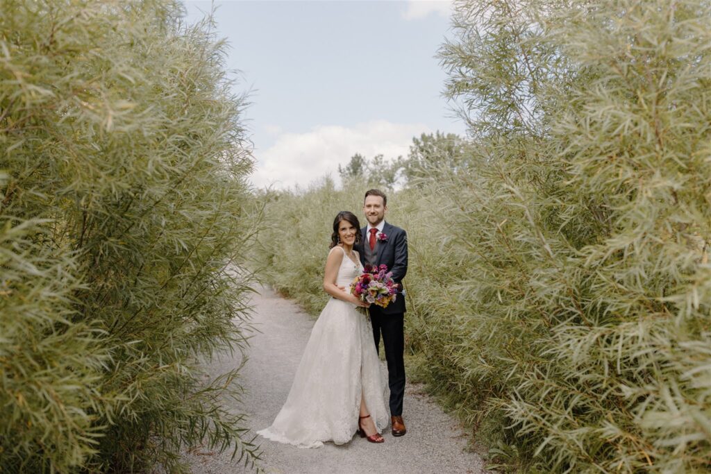 Maria and John post in the garden at their Toronto wedding. Maria wears a lace wedding dress with slit by Astrid & Mercedes