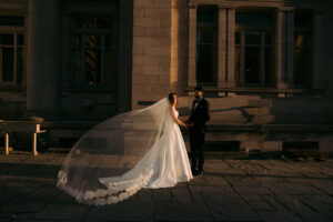 Bride and groom holding hands in golden hour light, bride wearing ballgown wedding dress with cathedral length lace veil