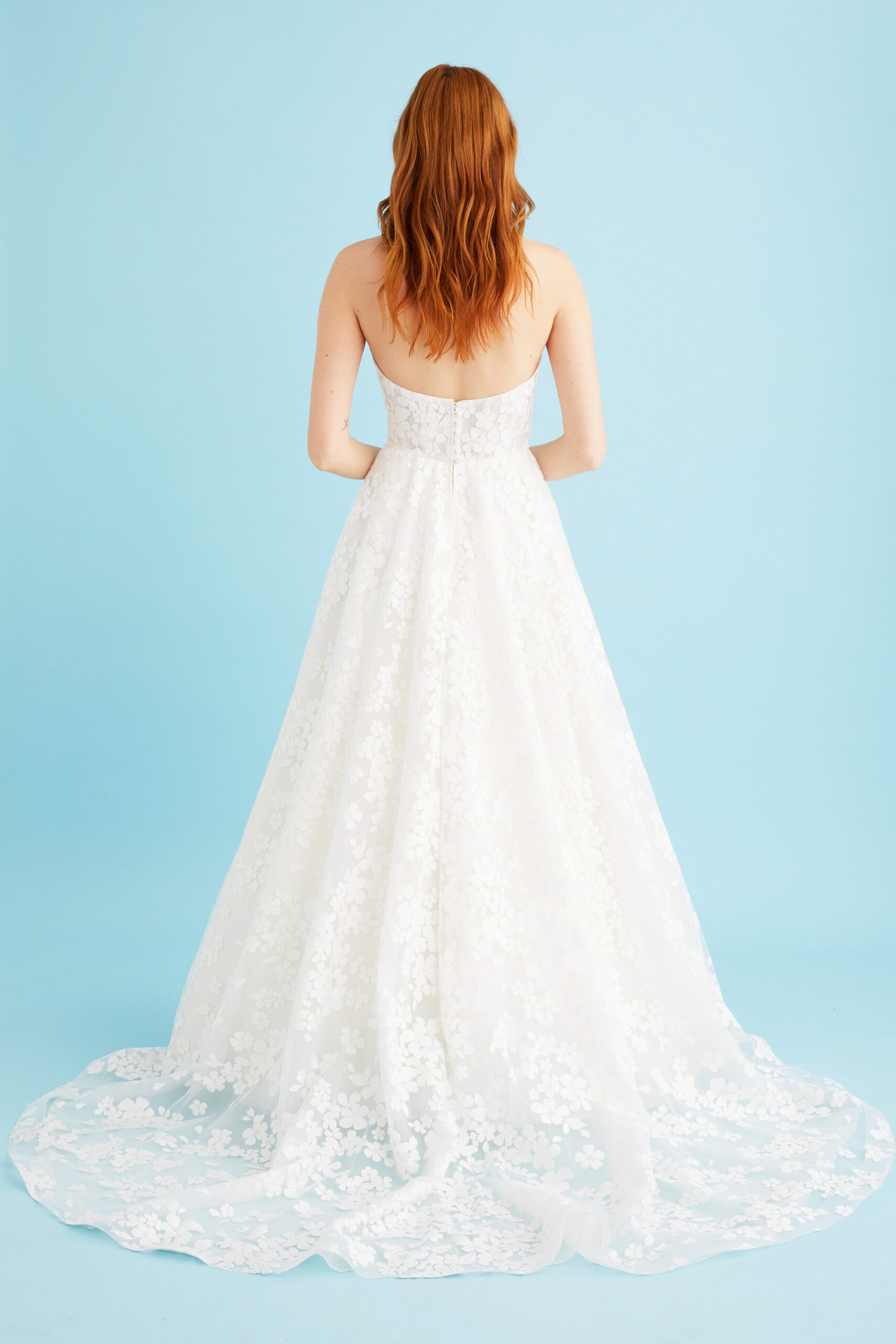 Back view of the Coralie wedding dress in off-white by Toronto wedding dress designer Lea-Ann Belter. The sheer corseted bodice meets a full circle skirt that flows into a translucent train with a button-and-loop closure.