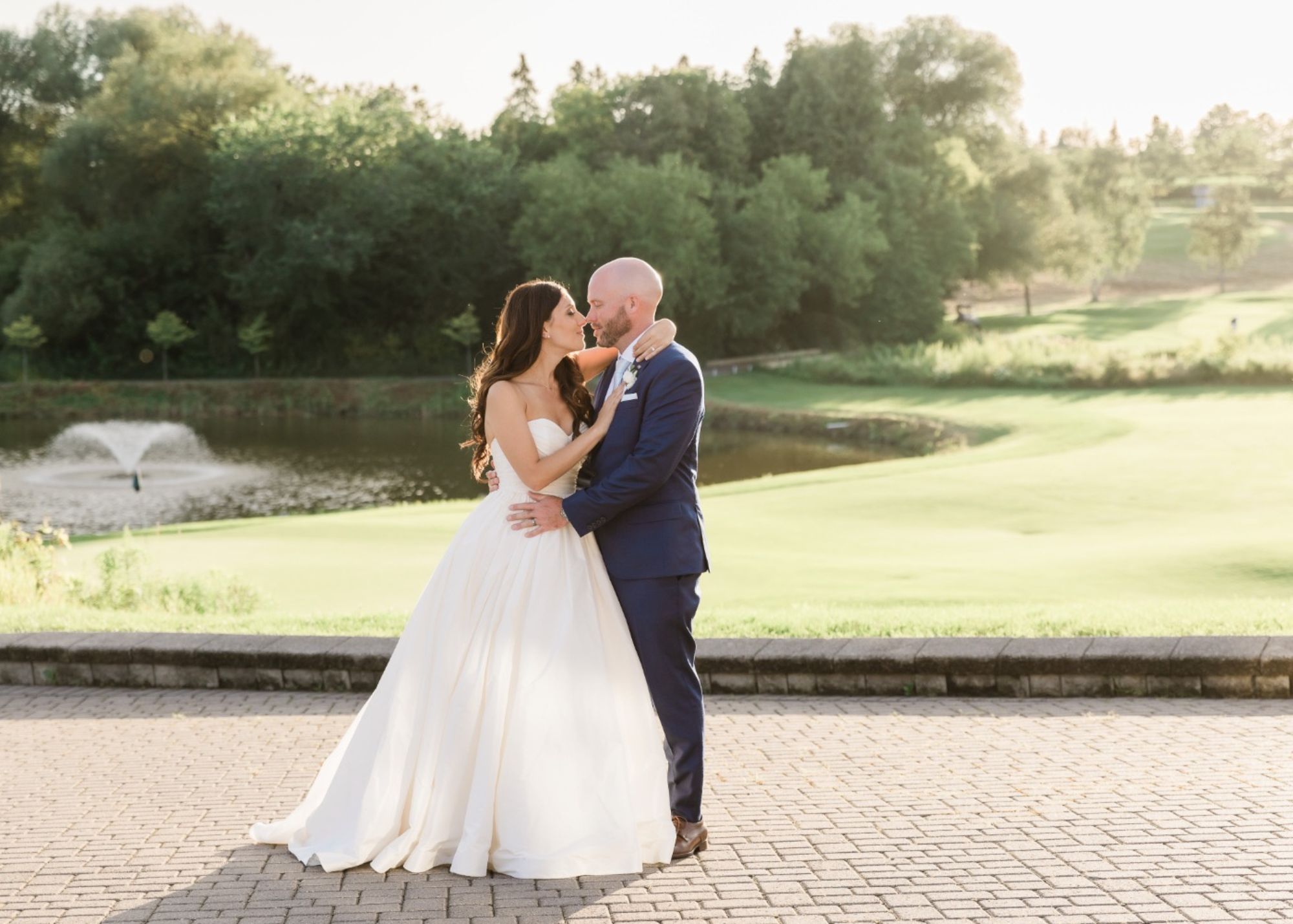 A bride and groom kiss in the afternoon sunshine. tThe bride wears a romantic wedding dress ball gown by Lea-Ann Belter Bridal.