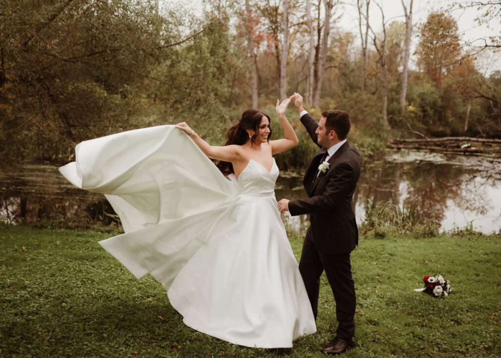 a bride twirls in her pointed sweetheart ball gown as her groom holds her hand in a fall meadow