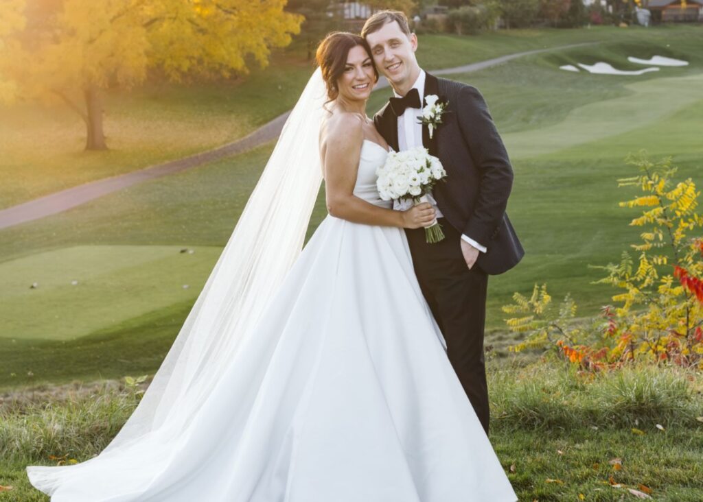A bride and groom hold each other, beaming at the golden hour. The bride wears a cathedral veil and custom wedding dress by Canadian bridal designer Lea-Ann Belter