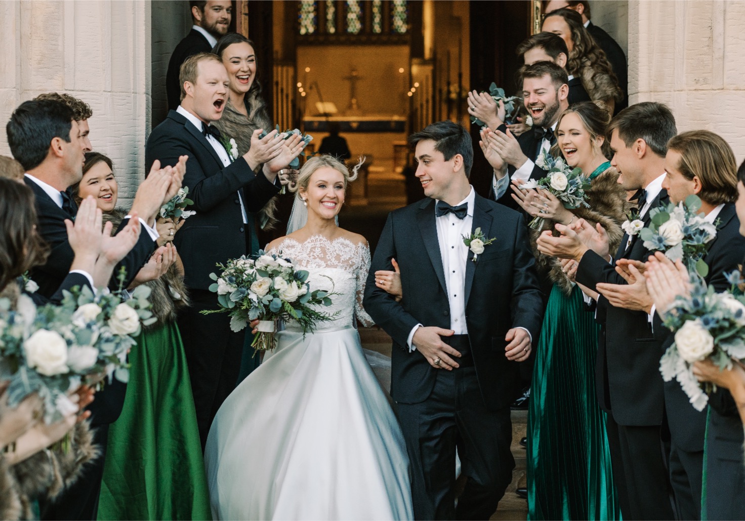 A bride and groom walk out of a church during their winter wedding , the bride is wearing a lace top and staples ball gown wedding dress