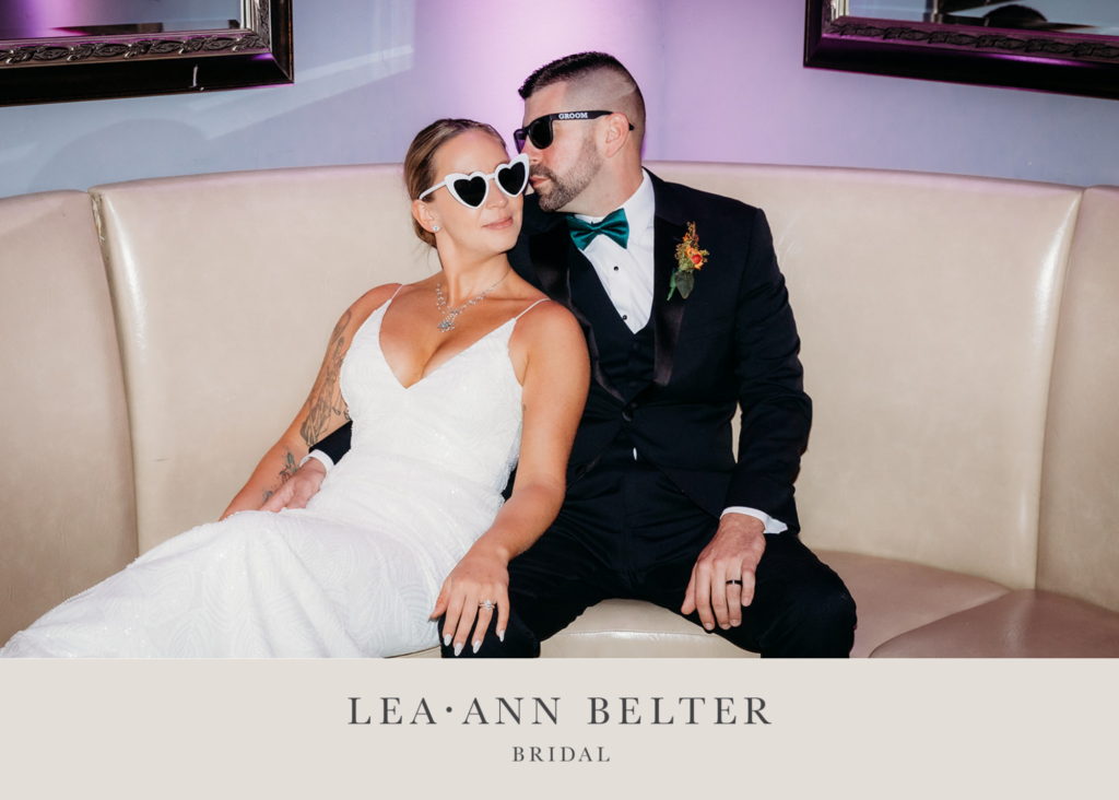 a bride and groom kiss on a white banquette. She's wearing a modern v neck wedding dress, he a tux.