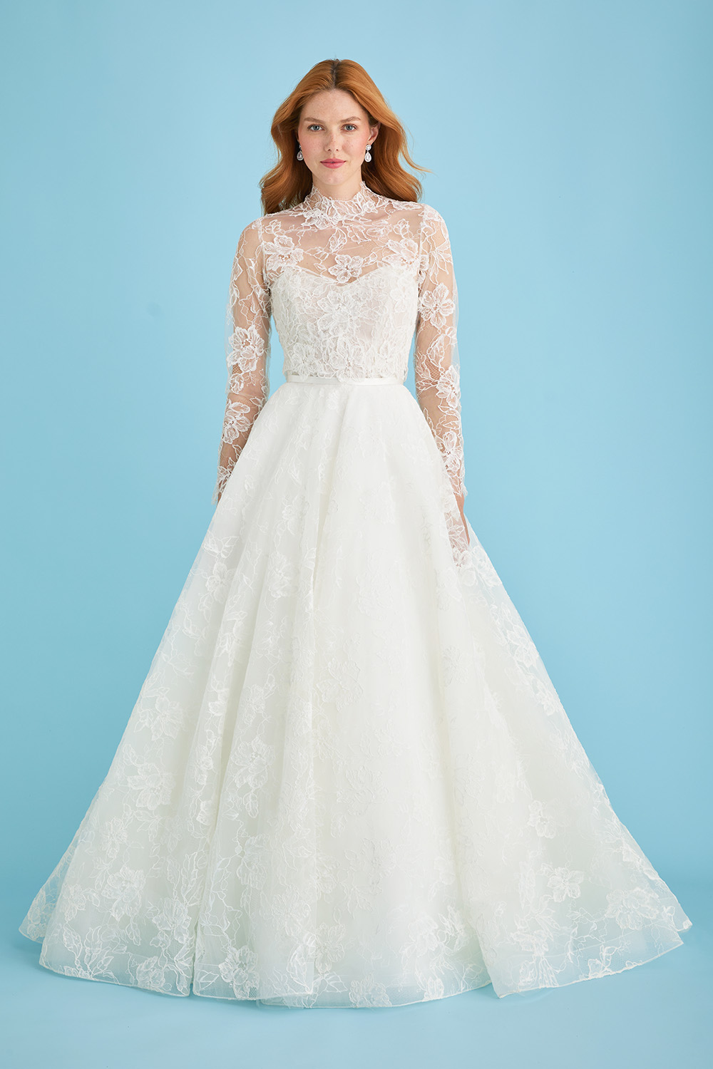 Bride wearing the Lea-Ann Belter Bridal Jane gown styled with a high-neck lace bridal jacket. The sheer overlay adds coverage and drama with long sleeves and floral detailing, creating a modest and elegant silhouette.