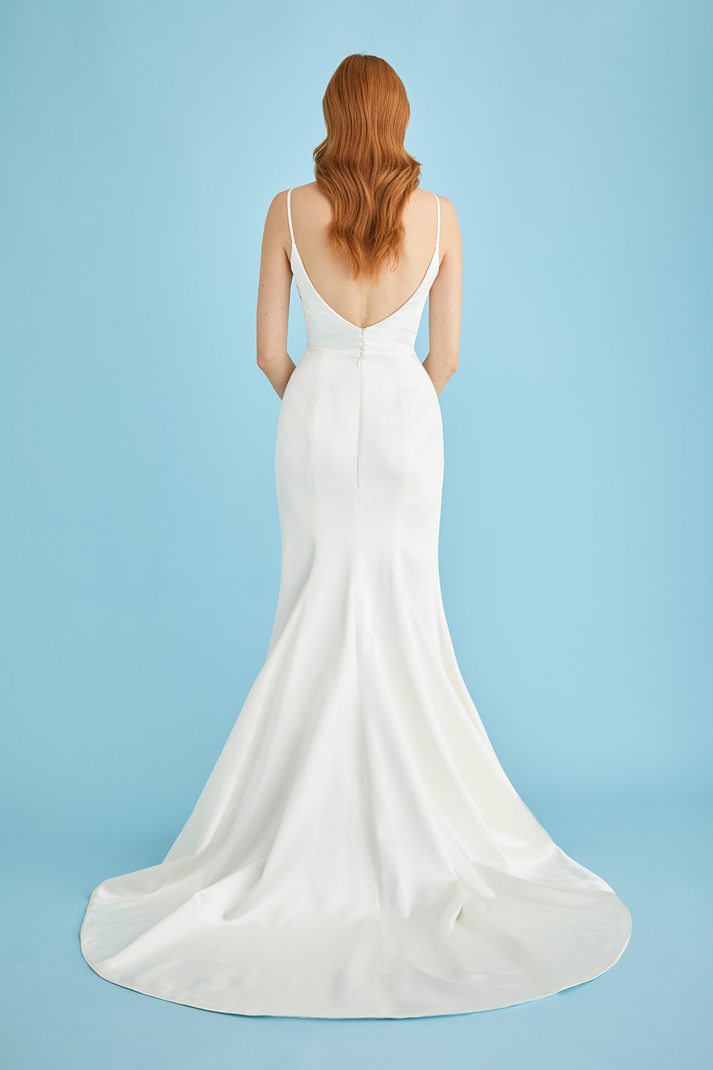 Bride wearing the Lila satin fit-and-flare wedding dress, shown from behind to highlight the low scoop back, slim spaghetti straps, and dramatic train.
