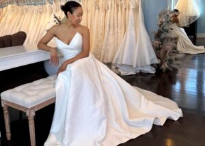a bride sits on a bench in a Toronto bridal shop wearing a wedding dress with pointed strapless neckline