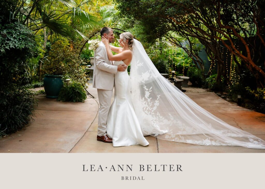 Bride in a strapless fit-and-flare wedding dress with a floral cathedral veil, embracing her groom in a lush garden setting.