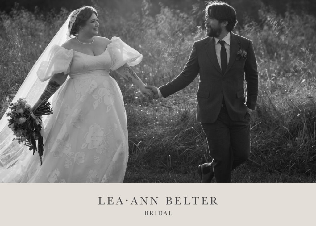 Bride Alaina in Lea-Ann Belter's floral Esperanza wedding dress with cathedral veil holds hands with groom Ian in loden suit during golden hour portraits at White Hall Vineyard