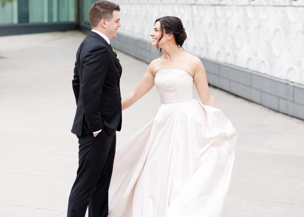 Bride in blush ballgown wedding dress twirling with groom at modern venue in soft natural light