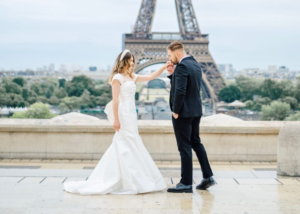 room kissing bride's hand at Trocadéro with Eiffel Tower in background, bride wearing Lea-Ann Belter fit-and-flare gown