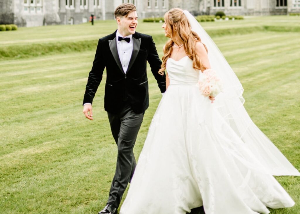 Joyful newlyweds laughing while walking across manicured lawn at estate, bride in ballgown with flowing skirt