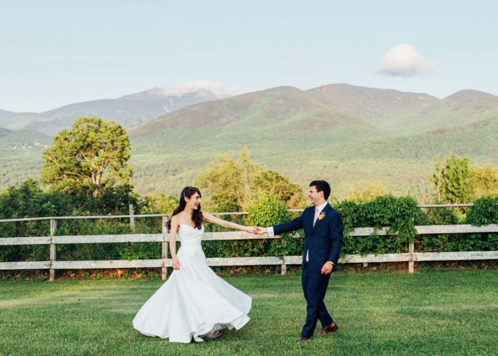 Bride in strapless Lea-Ann Belter ballgown dancing with groom against mountain backdrop at rustic outdoor venue