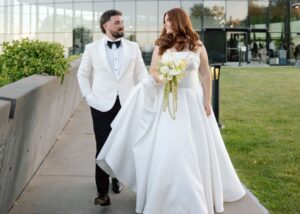 Jaqueline and Matthew walk outside together, Matthew holds the train of his bride's ball gown wedding dress