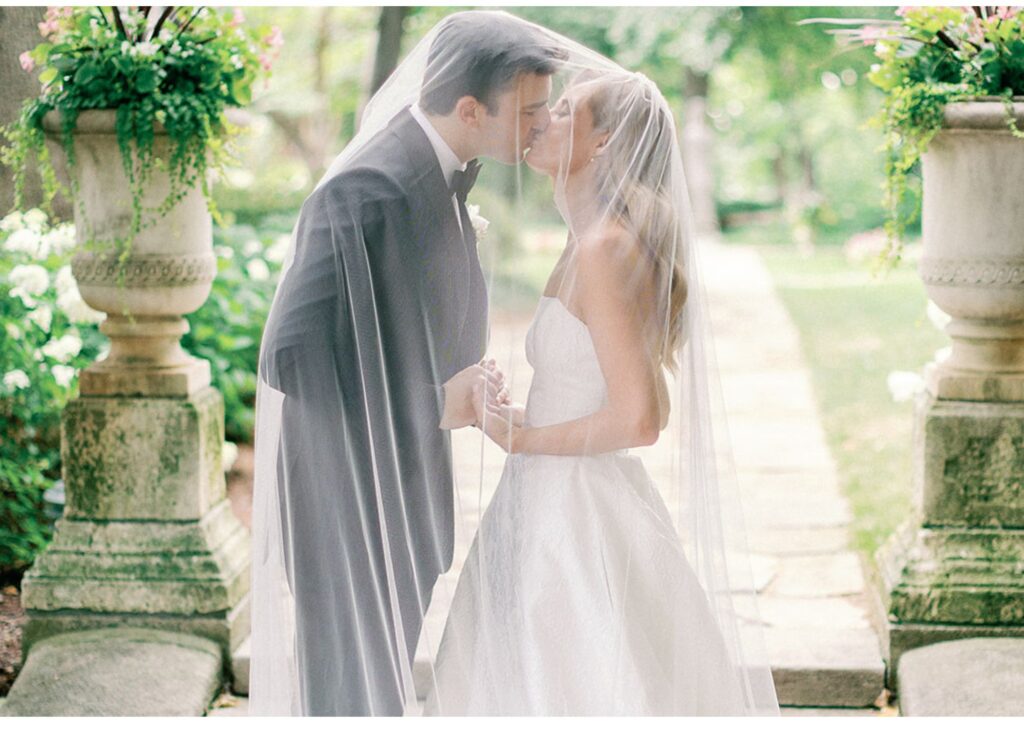 A bride and groom kiss under the bride's veil in the lush gardens at Meridian House in Washington, DC