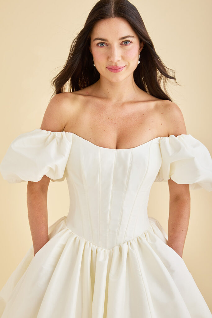 Etoile bridal gown featuring cat eye neckline, off-the-shoulder puff sleeves, Basque waist corseted bodice, and full ball gown skirt
