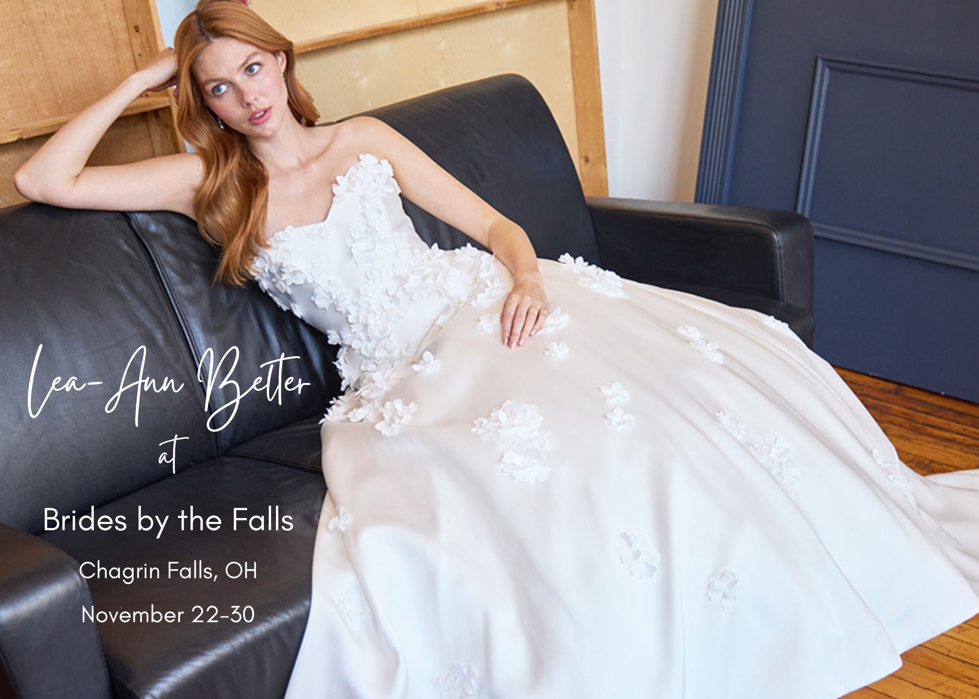Bride in romantic Lea-Ann Belter wedding gown with 3D floral appliqués and tulle skirt, reclining on black leather sofa. Text reads: Lea-Ann Belter at Brides by the Falls, Chagrin Falls, OH, November 22-30