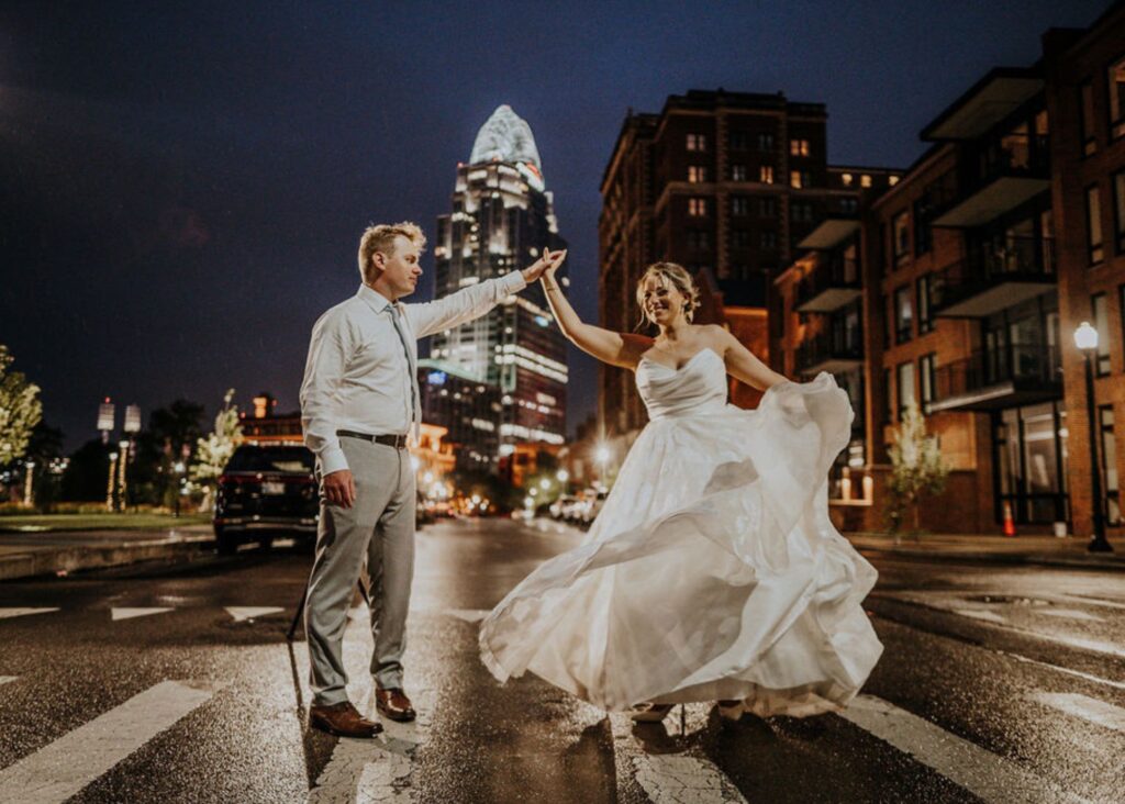 A bride ad groom dance in a street at night. The groom twirls the bride, sending her A-line skirt swirling.