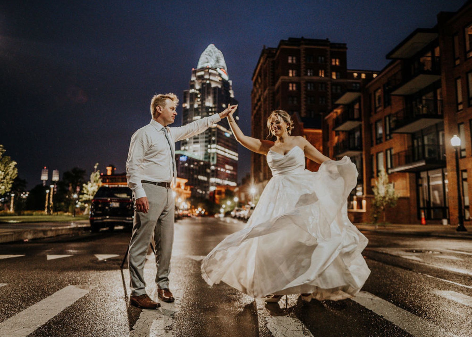 A bride ad groom dance in a street at night. The groom twirls the bride, sending her A-line skirt swirling.