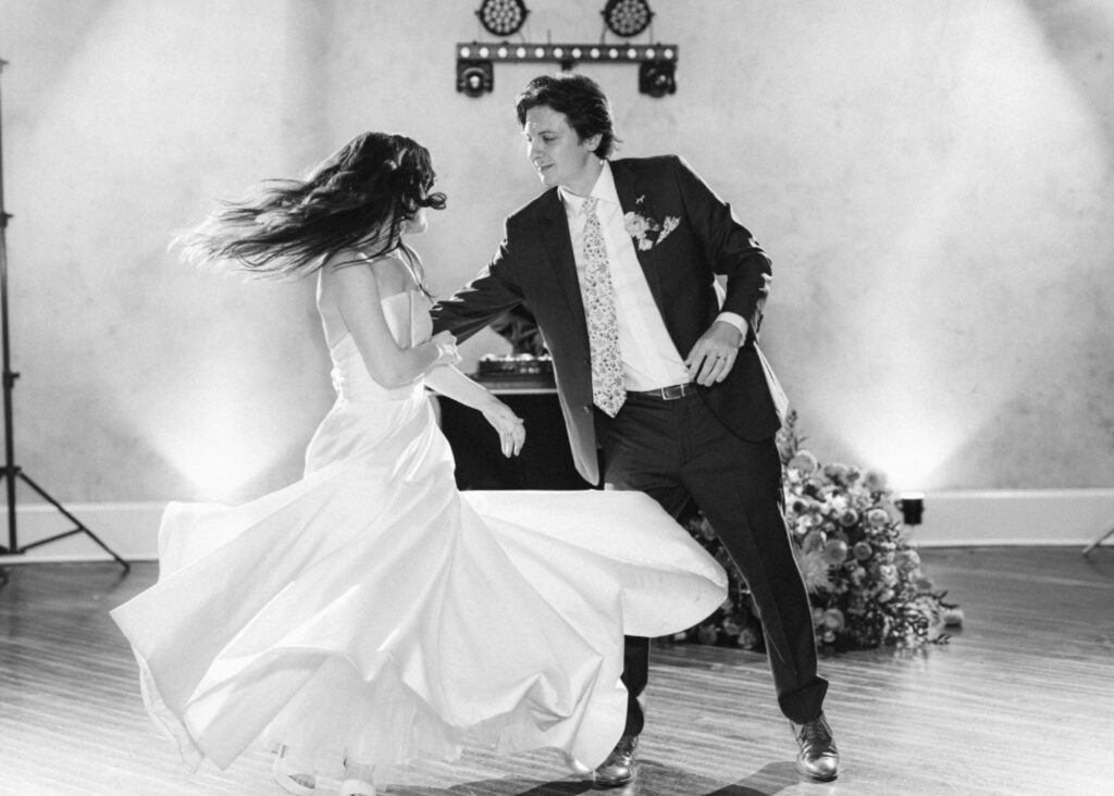 A groom twirls is bride on the dance floor. The bride wears her Astrid & Mercedes Vivid ballgown wedding dress.