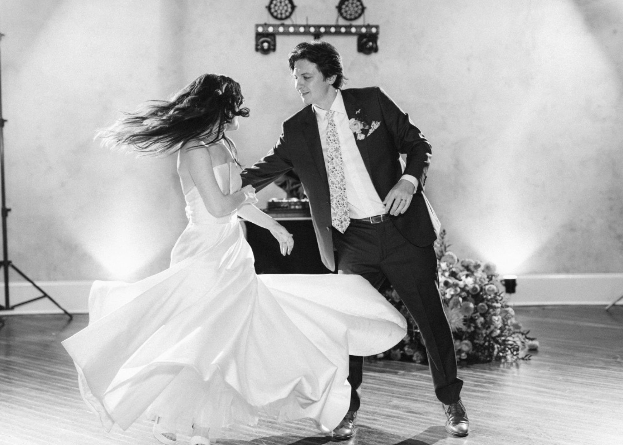 A groom twirls is bride on the dance floor. The bride wears her Astrid & Mercedes Vivid ballgown wedding dress.