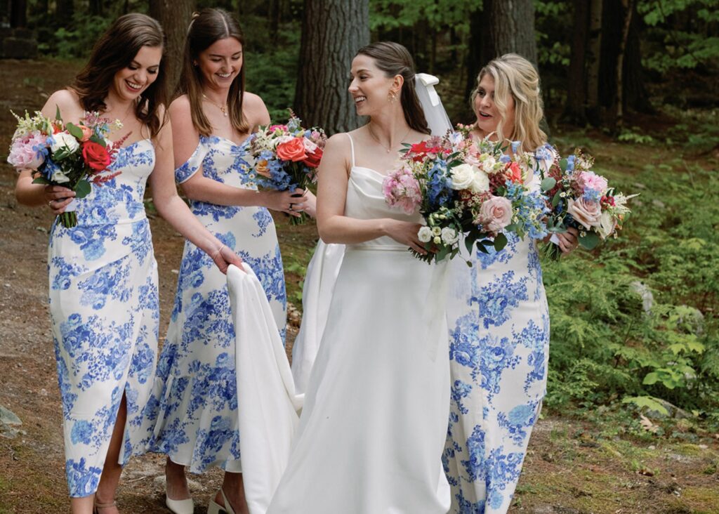 A bride wearing a sleek wedding dress walks with her bridesmaids wedding blue and white toile bridesmaids dresses through the woods.