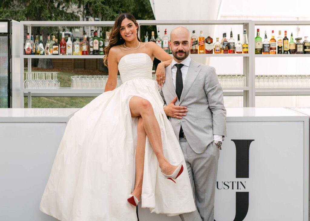 Bride in strapless ball gown sits on bar with crossed legs revealing skirt slit, groom in navy suit at Eaton Hall Inn wedding
