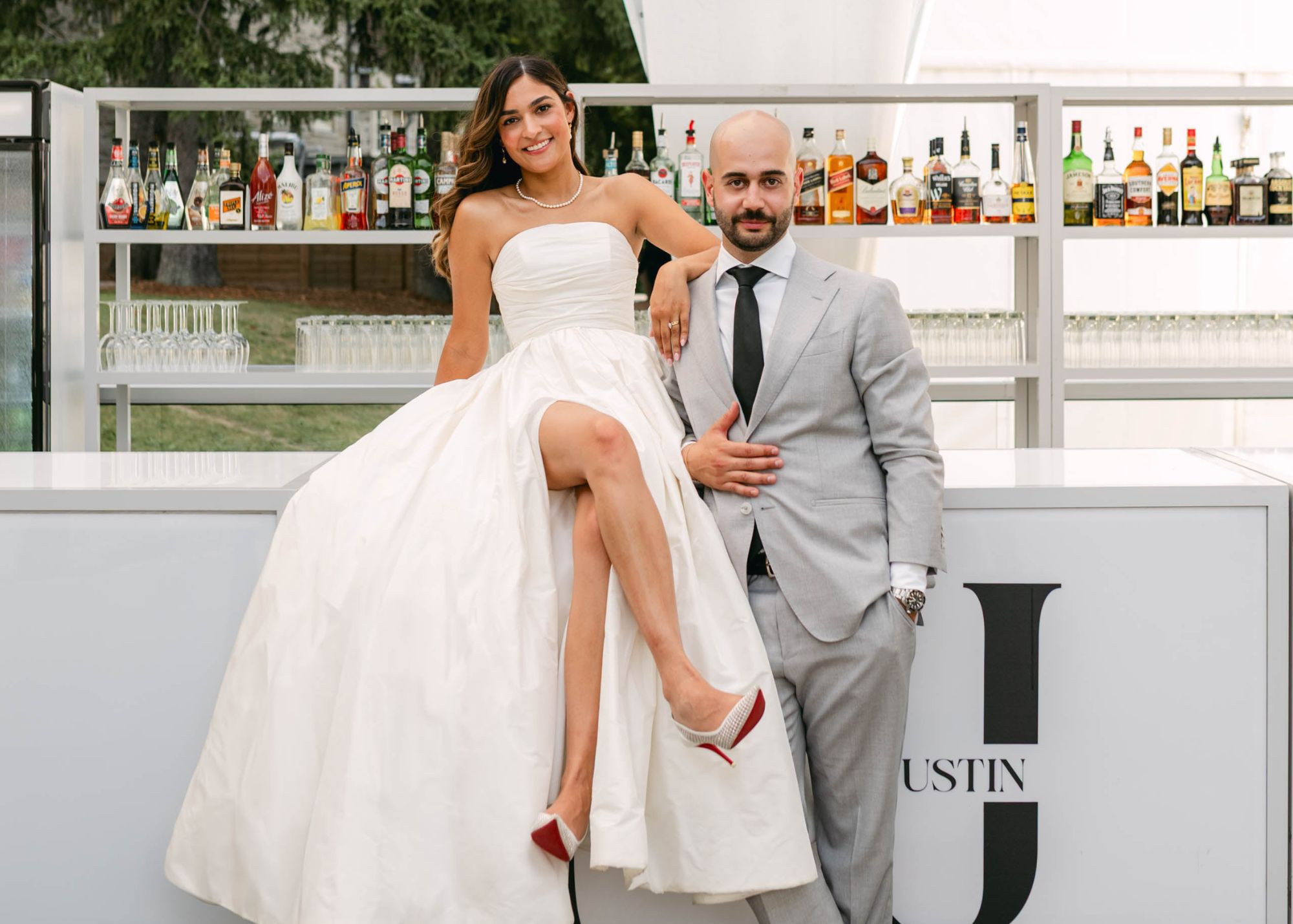 Bride in strapless ball gown sits on bar with crossed legs revealing skirt slit, groom in navy suit at Eaton Hall Inn wedding
