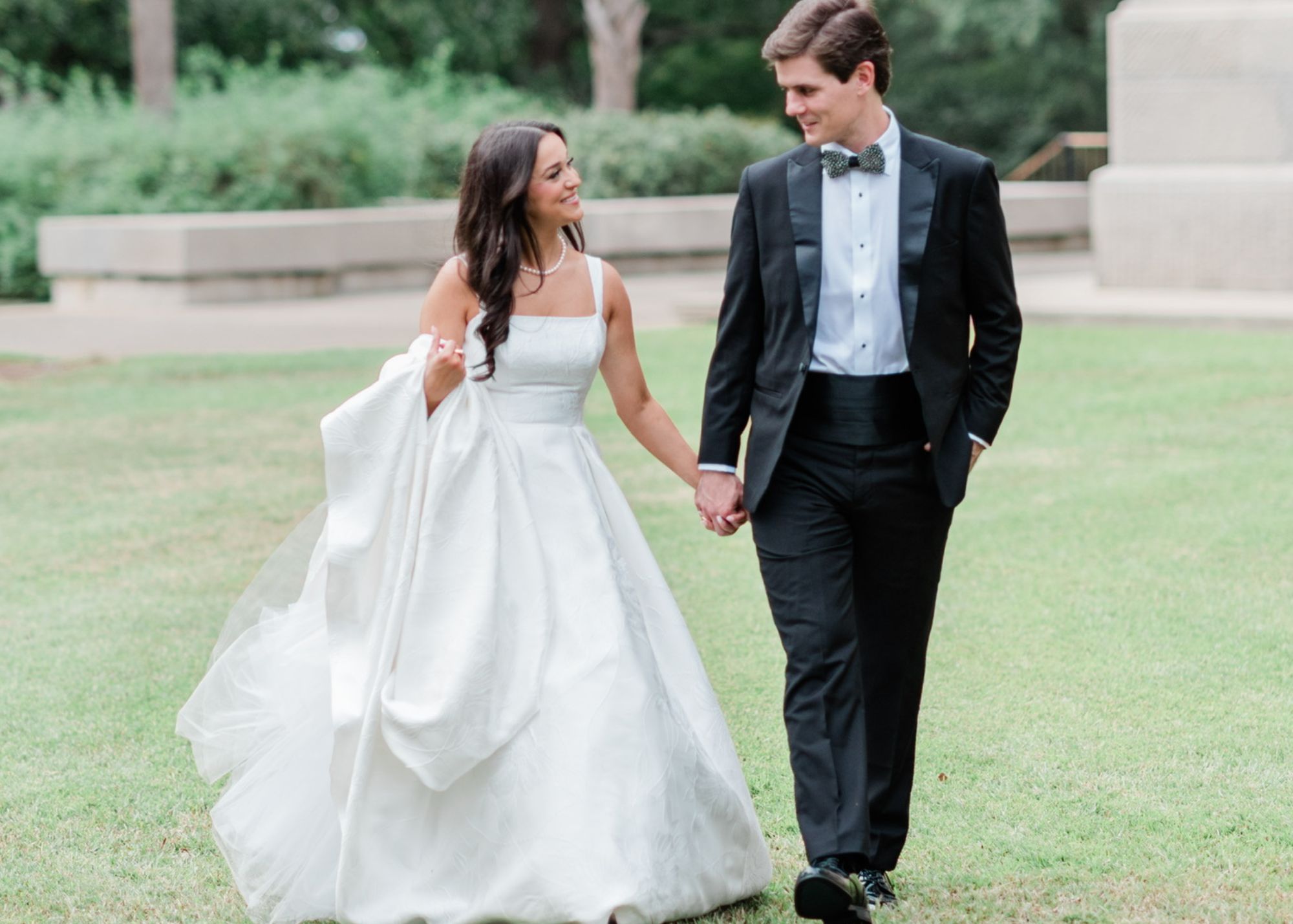 Bride and groom walk together on lawn at The Palmetto Club, bride wearing elegant white ball gown with off-shoulder sleeves