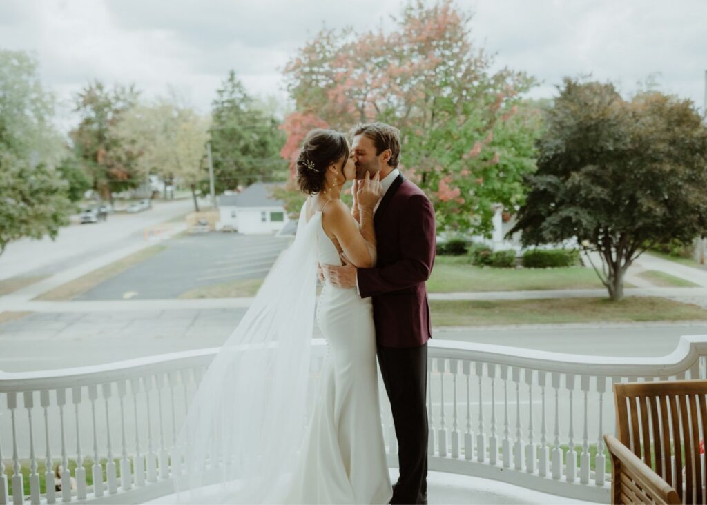 A bride and groom kiss in profile, her sheer, detachable cape train flutters. behind her, highlighting the romance and her gown's sleek shape.