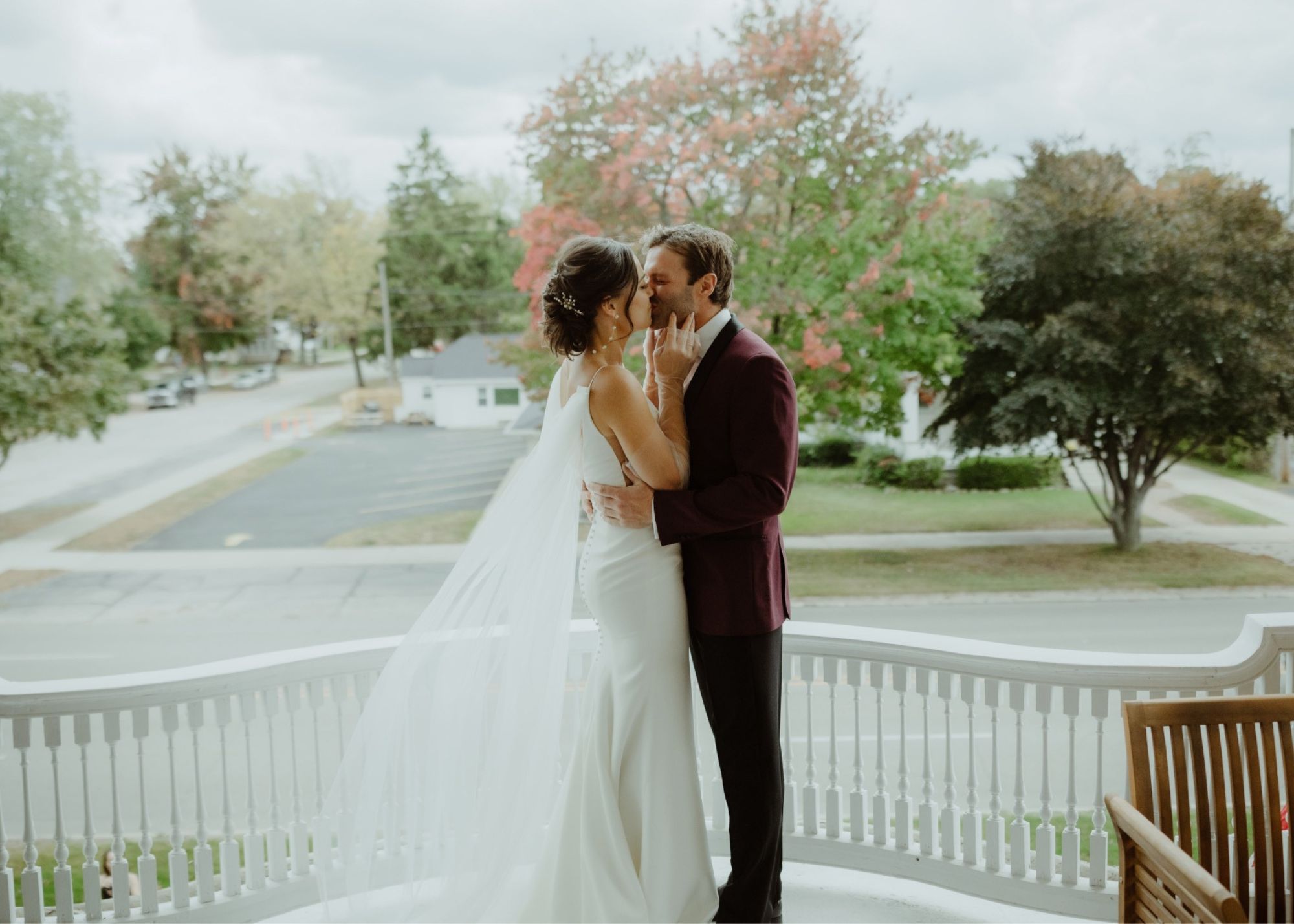 A bride and groom kiss in profile, her sheer, detachable cape train flutters. behind her, highlighting the romance and her gown's sleek shape.