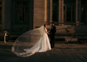 Bride and groom holding hands in golden hour light, bride wearing ballgown wedding dress with cathedral length lace veil