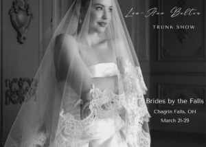 A close up of a bride wearing a classic drop waist ball gown and lace edged cathedral veil in black and white. Text reads - Lea-Ann Belter Keepsake collection trunk show, April 11-20 at Persnickety Bride in Newtown, Connecticut