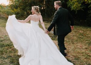 A bride and groom walk into the sunset, the bride swirls the full skirt of her ballgown wedding dress.