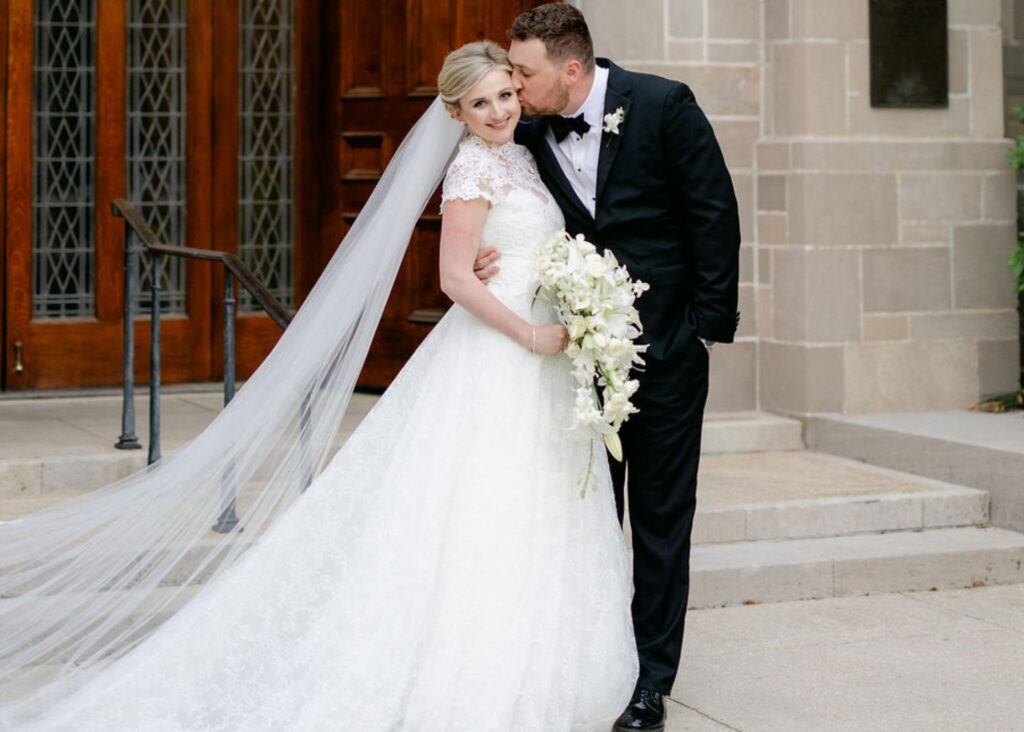 Real bride Madden in her lace Paradise lace ball gown and cathedral veil with her groom on the steps of their New Orleans church