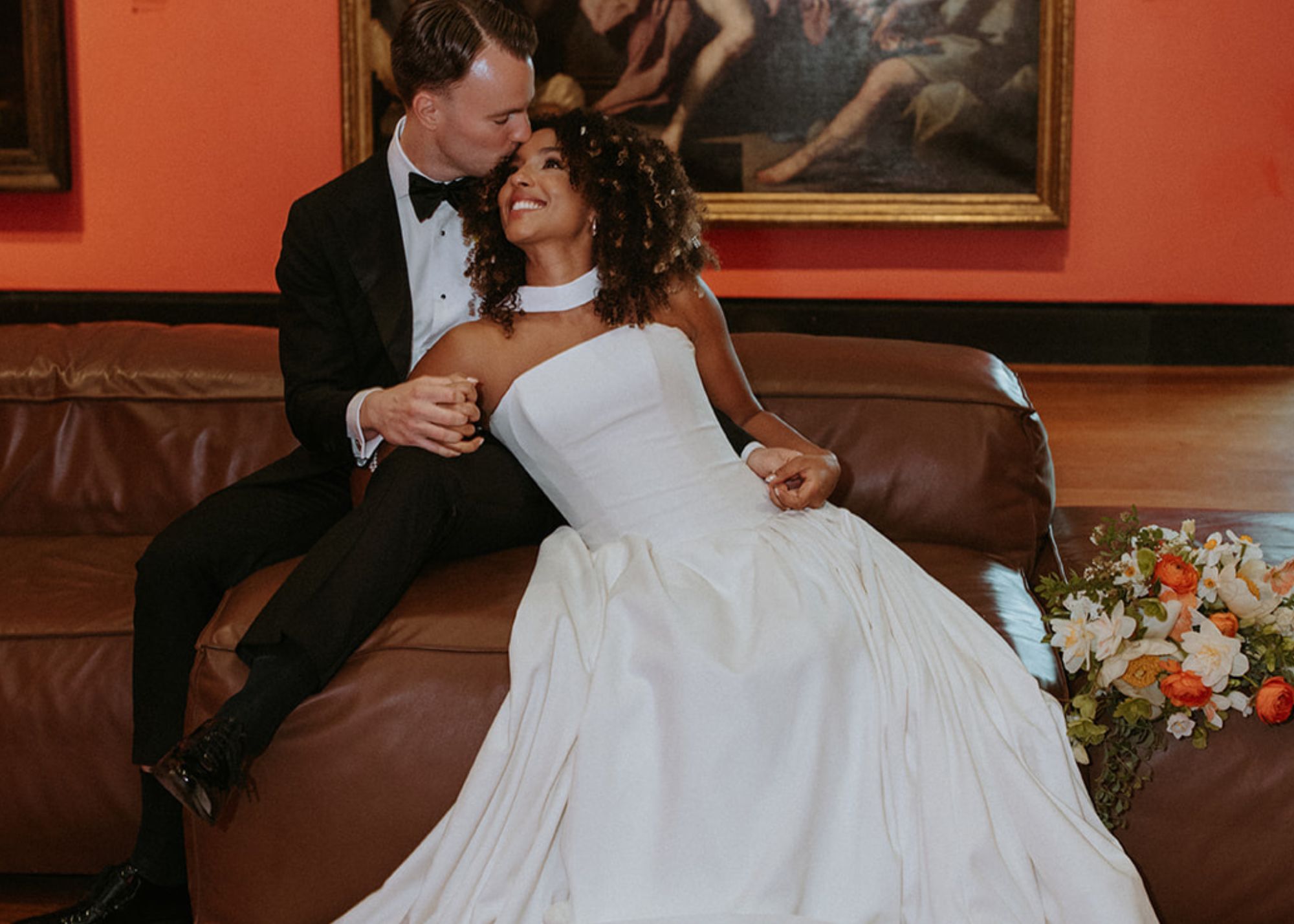 A bride wearing a modern drop waist ball gown of fluid crepe leans into her groom within the dramatic halls of the Art Gallery of Ontario.