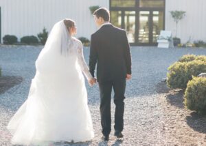 a bride and groom walk away in th golden afternoon sun, her lace ball gown and cathedral veil glow in the sunshine.