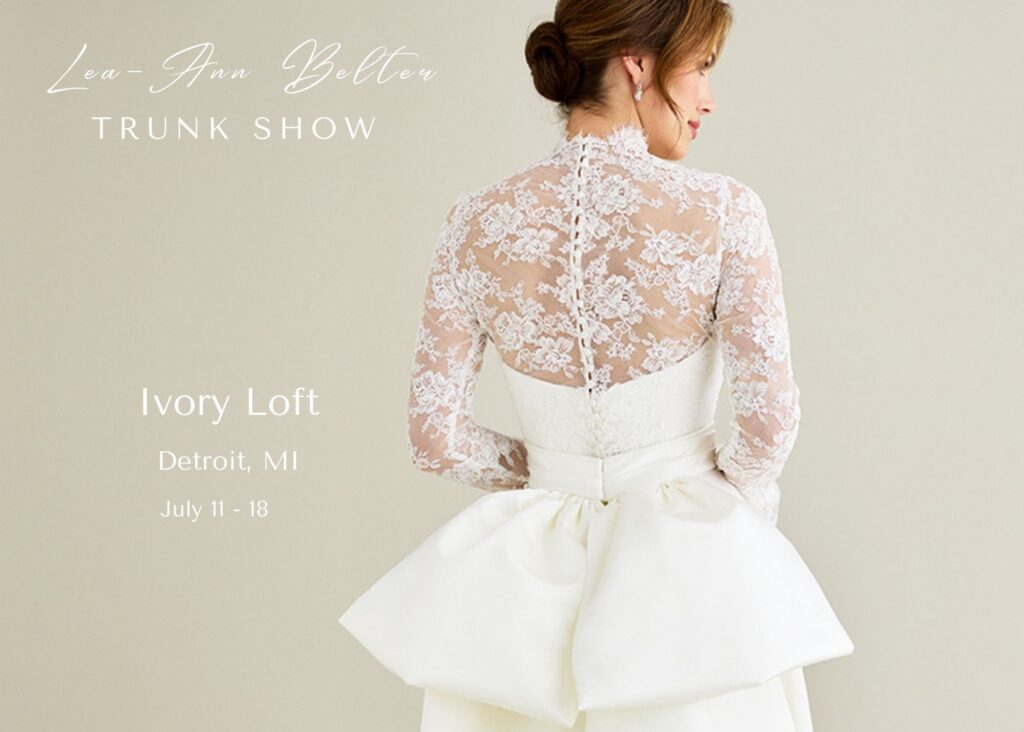 A bride in a sheer lace jacket and a wedding gown with back bow stands with her back to the camera. Text reads, Lea-Ann Belter Truk show, Ivory Loft Bridal, Detroit, MI, July 8-11
