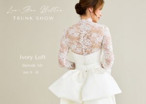 A bride in a sheer lace jacket and a wedding gown with back bow stands with her back to the camera. Text reads, Lea-Ann Belter Truk show, Ivory Loft Bridal, Detroit, MI, July 8-11