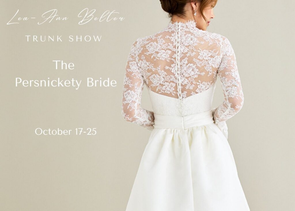 Close-up of the back of a bride in a bridal gown with lace top and dramatic, long tails. Text reads: Lea-Ann Belter Bridal trunk show, 2027 Sea Glass collection at the Persnickety Bride, Newton CT, October 17-25