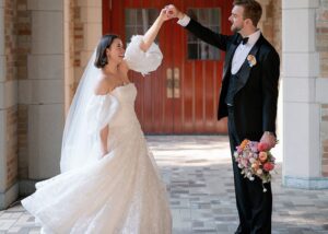 a bride pirouettes as her groom holds her hand. The bride wears a laser cut floral drop waist ball gown wedding dress with detachable puff sleeves by Lea-Ann Belter, the groom a tux.