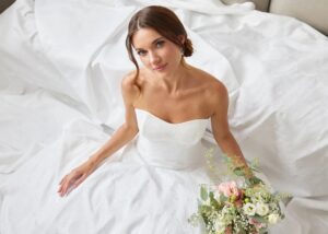 The Sandy wedding dress by Astrid & Mercedes, a floral jacquard gown with a sweetheart neckline and full skirt, worn by a seated bride