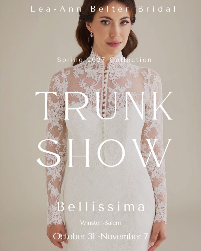 A bride wearing a sheath dress and sheer lace long sleeved bridal jacket that buttons up the front. Text overlay reads: Lea-Ann Belter Bridal trunk show at Bellissima, Winston Salem, Oct 30-November 7
